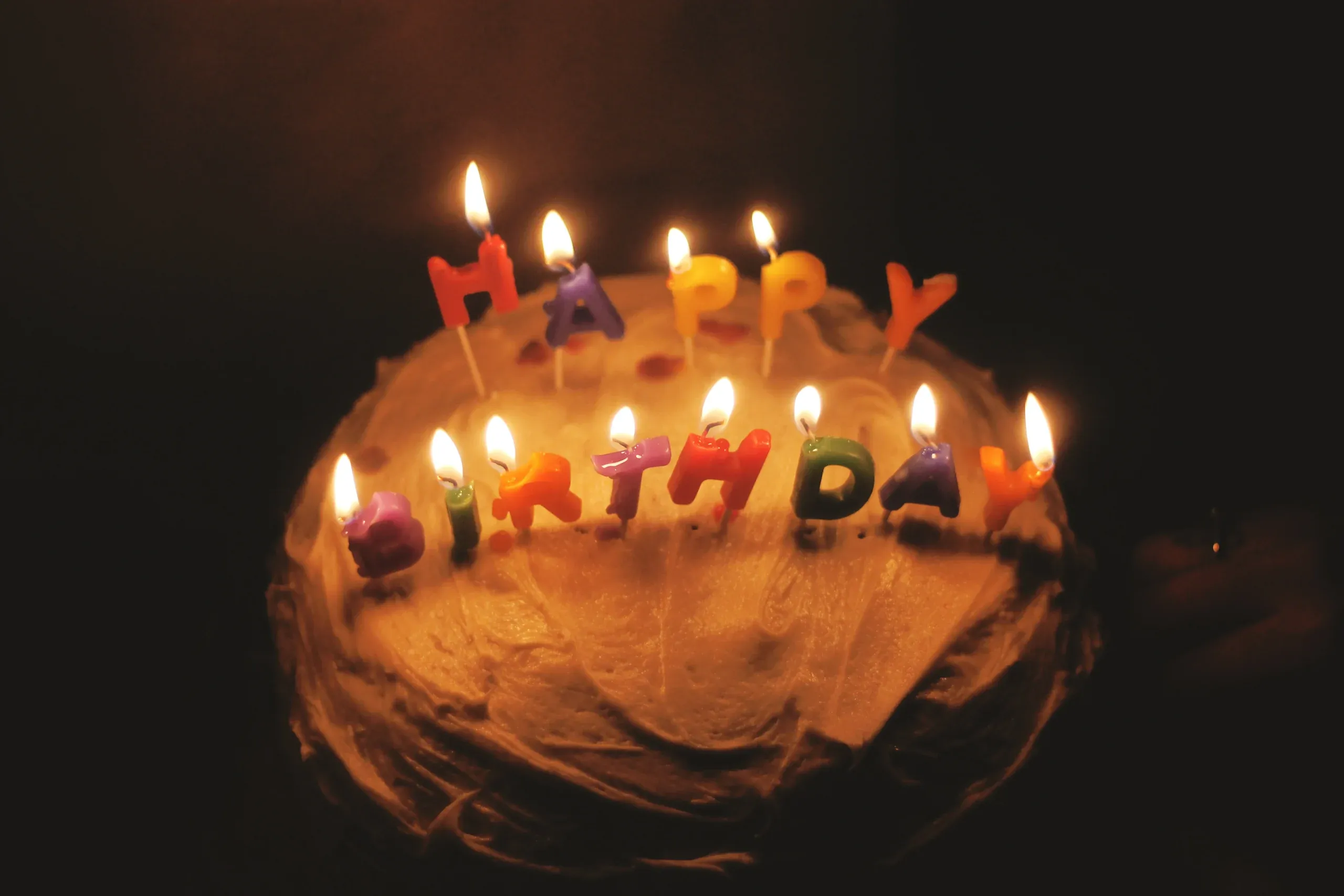 A birthday cake glowing with lit letter candles in a dark room