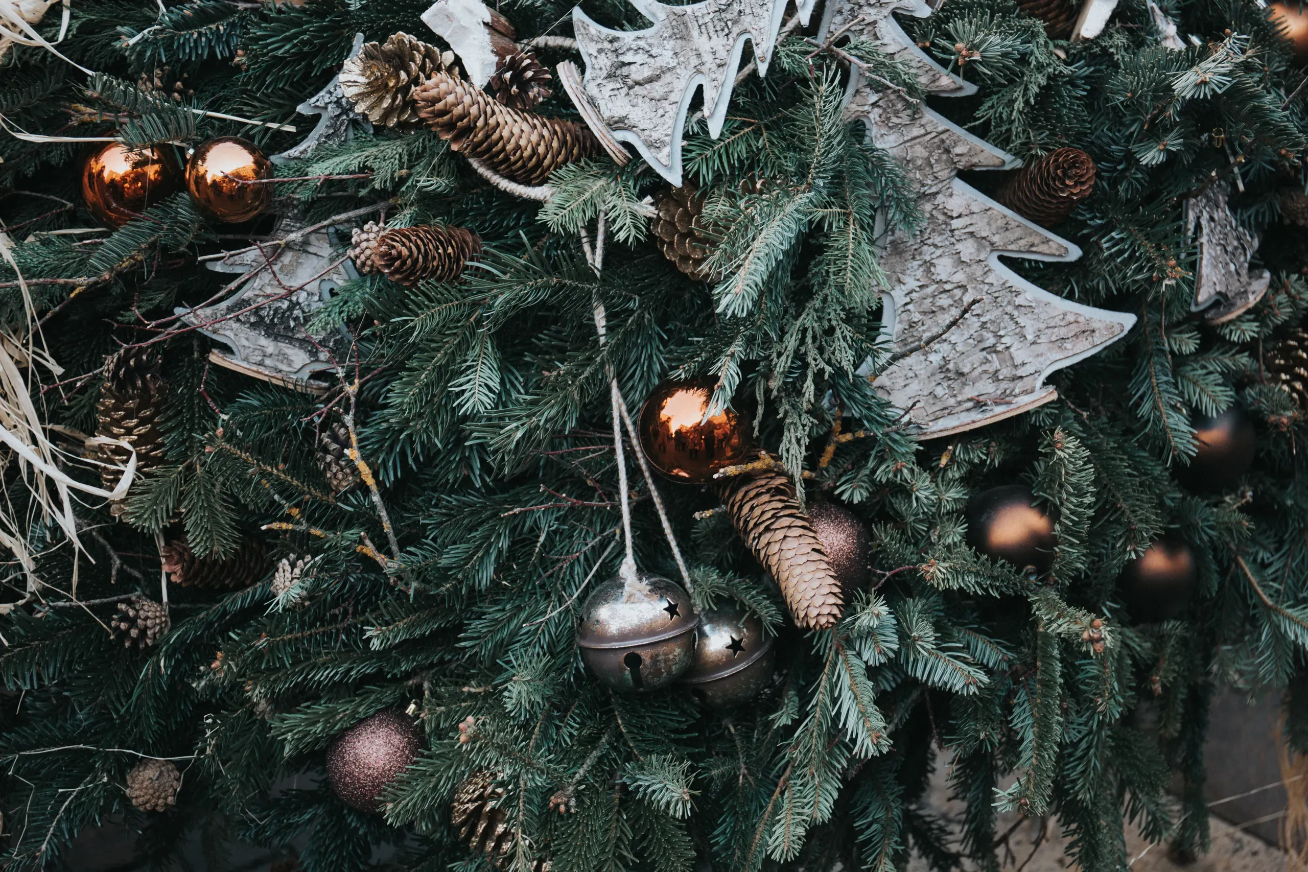 Pine cones, bells and paper decorations hanging on the branches of a Christmas tree