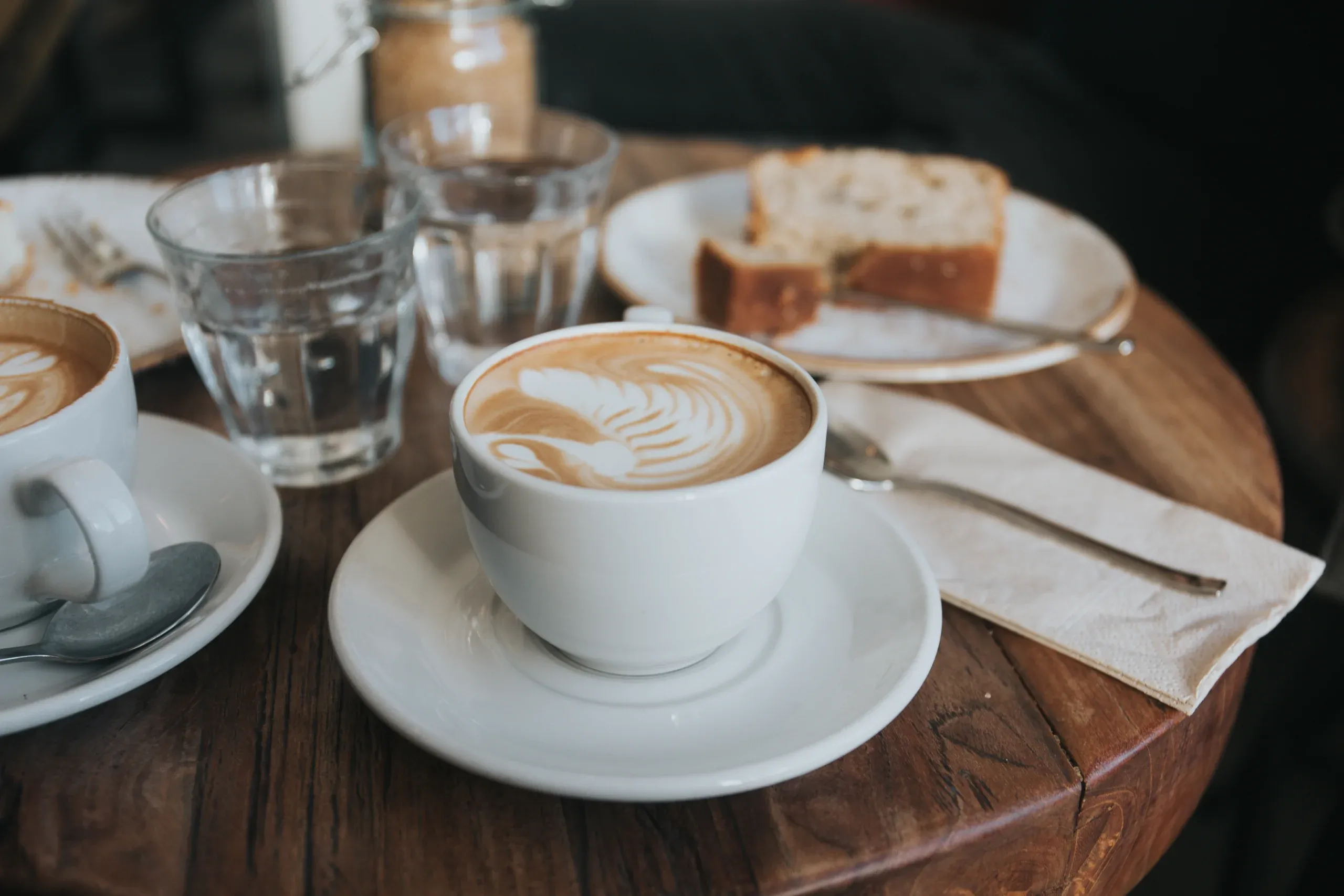 Cappuccinos and slices of cake on a round timber table