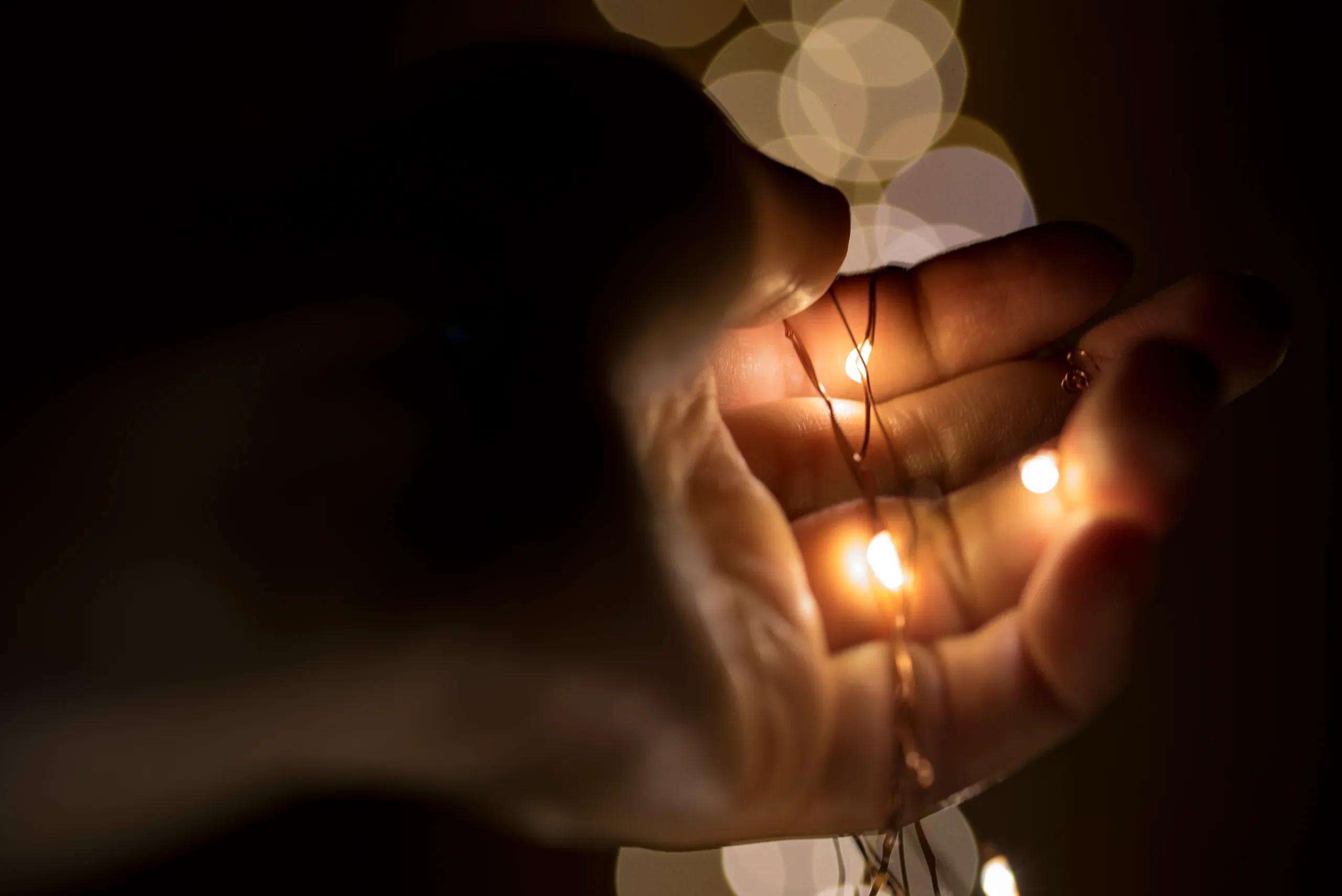 A cupped hand holding a strand of warm fairy lights in the dark