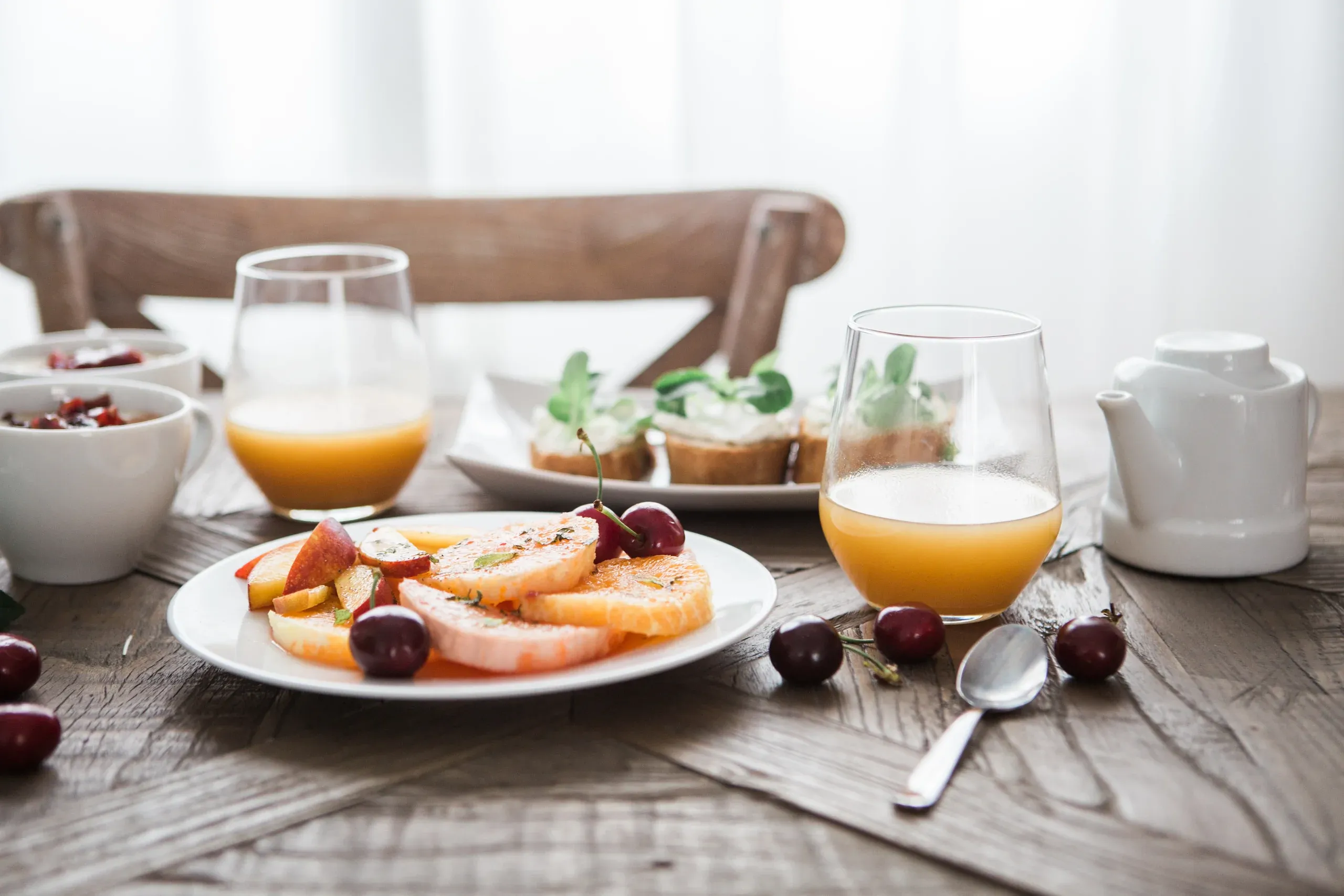 A sunny table with fresh fruit, orange juice and small plates on timber