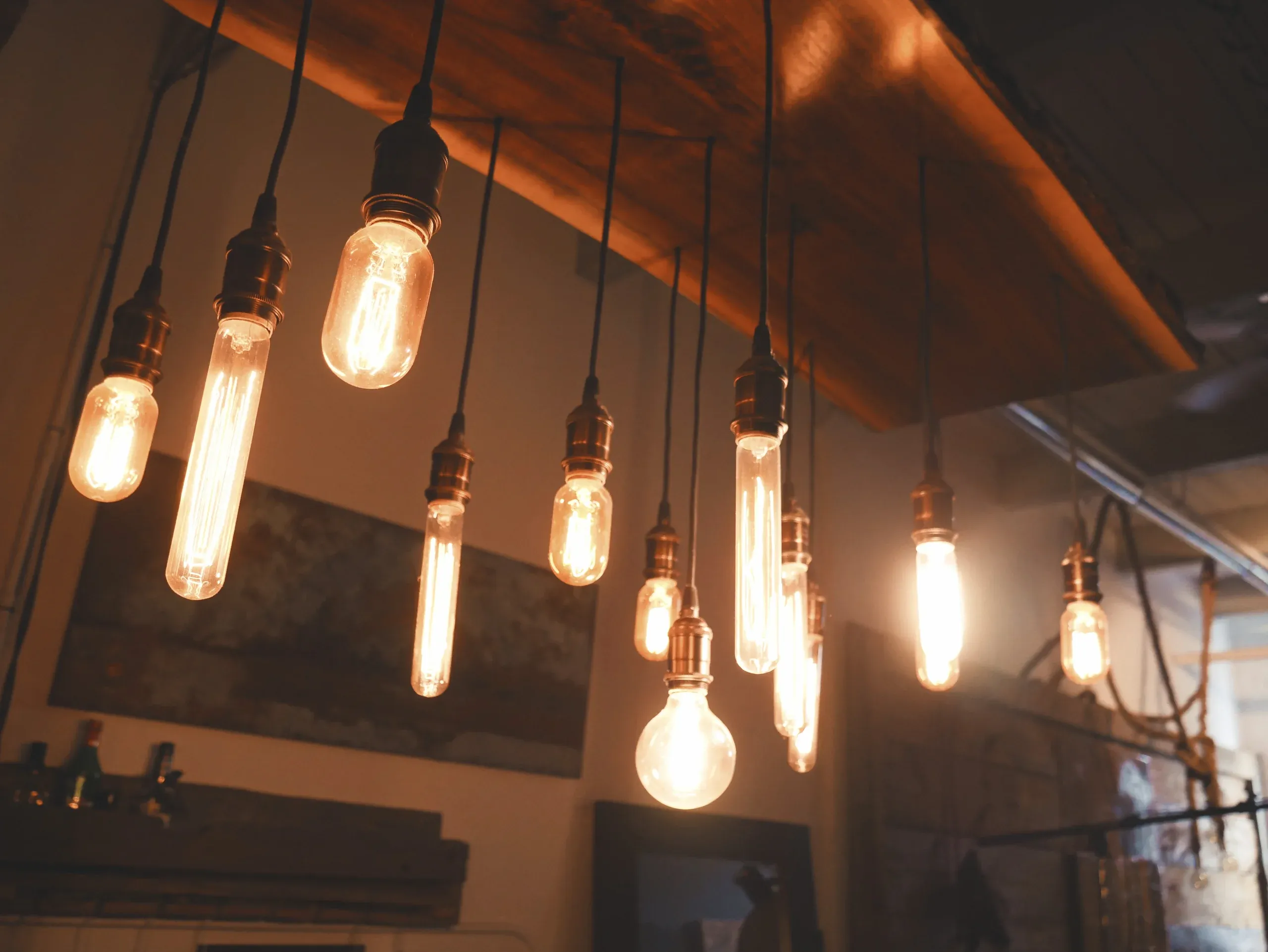 Filament bulbs hanging at different heights beneath a timber ceiling beam